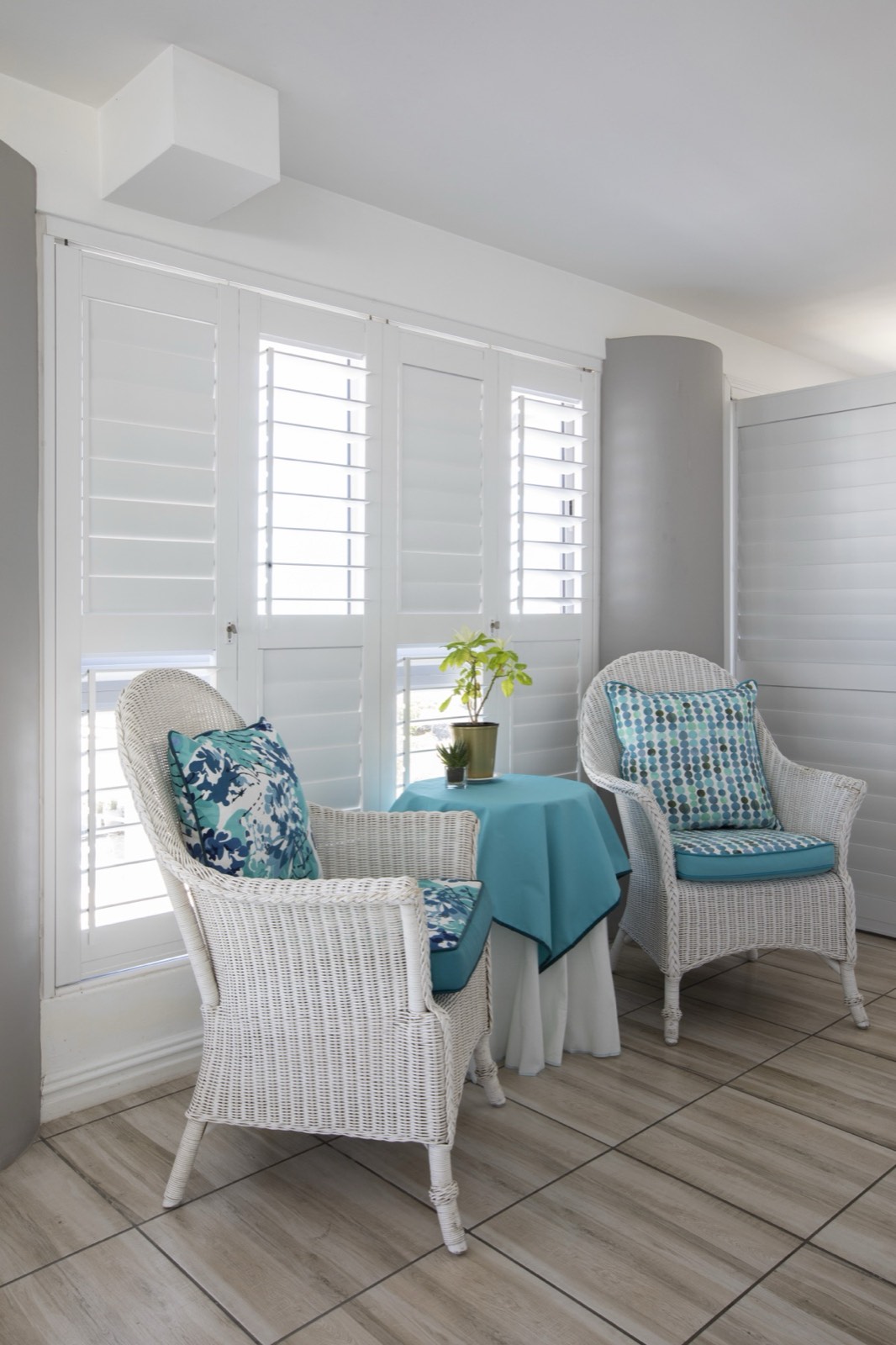 White aluminium shutters closing off a sunroom with wicker chairs
