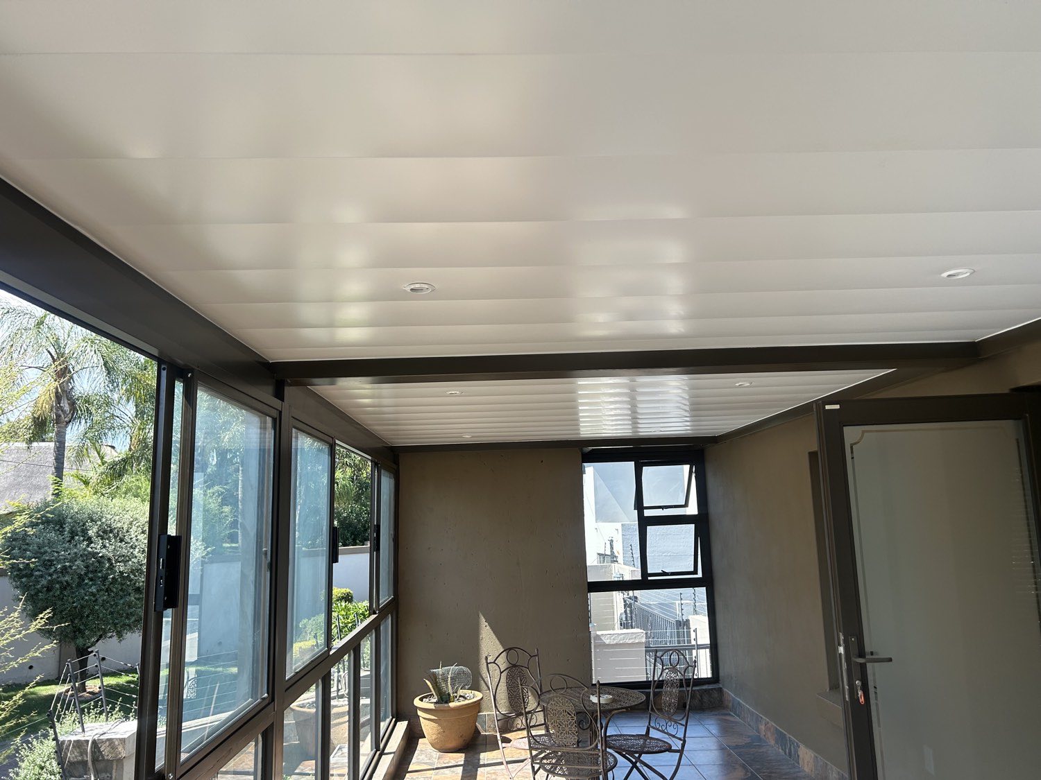 White ceiling panels with downlights inside a bronze-framed patio enclosure