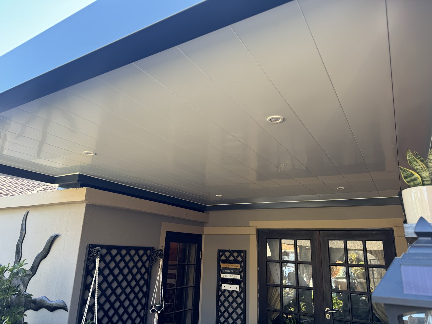 Warm-grey ceiling panels with recessed downlights under a charcoal fascia over an entrance patio