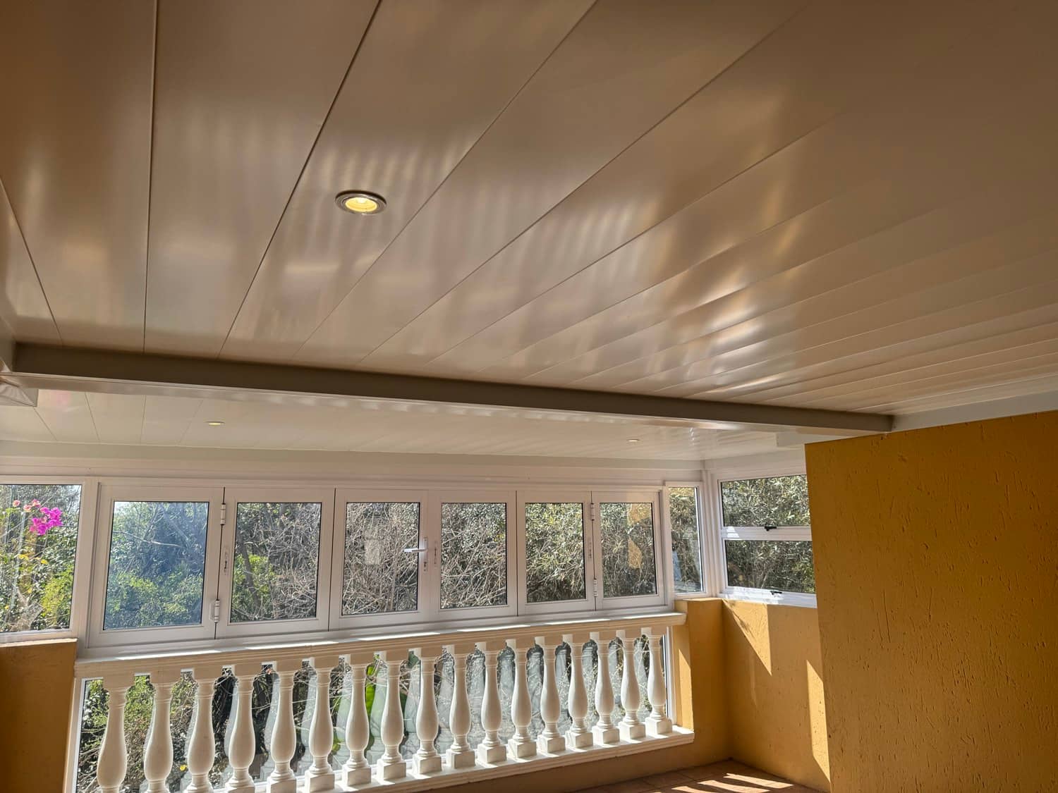 White panel ceiling with a recessed downlight over an enclosed balcony with a white balustrade