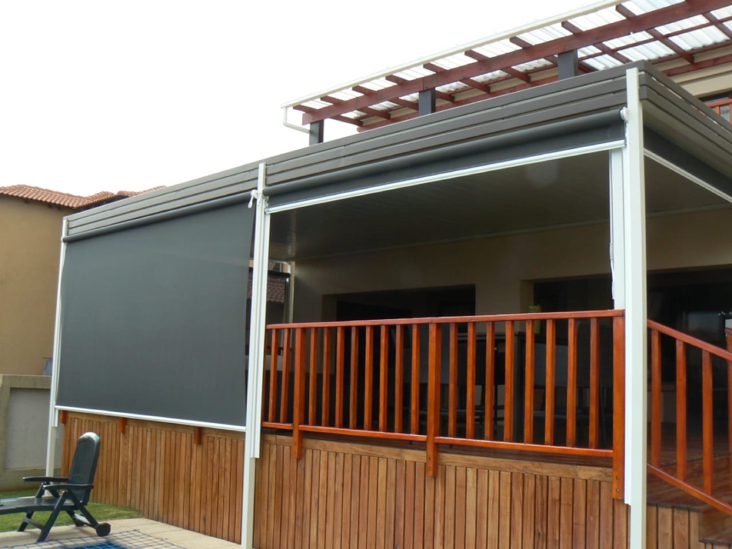 Two charcoal drop blinds lowered under a grey fascia on a raised patio with a wooden balustrade