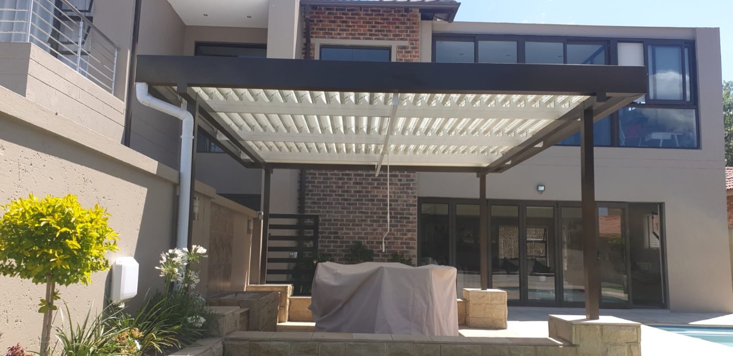Bronze aluminium louvre pergola attached to a modern double-storey home shading a stone-edged patio
