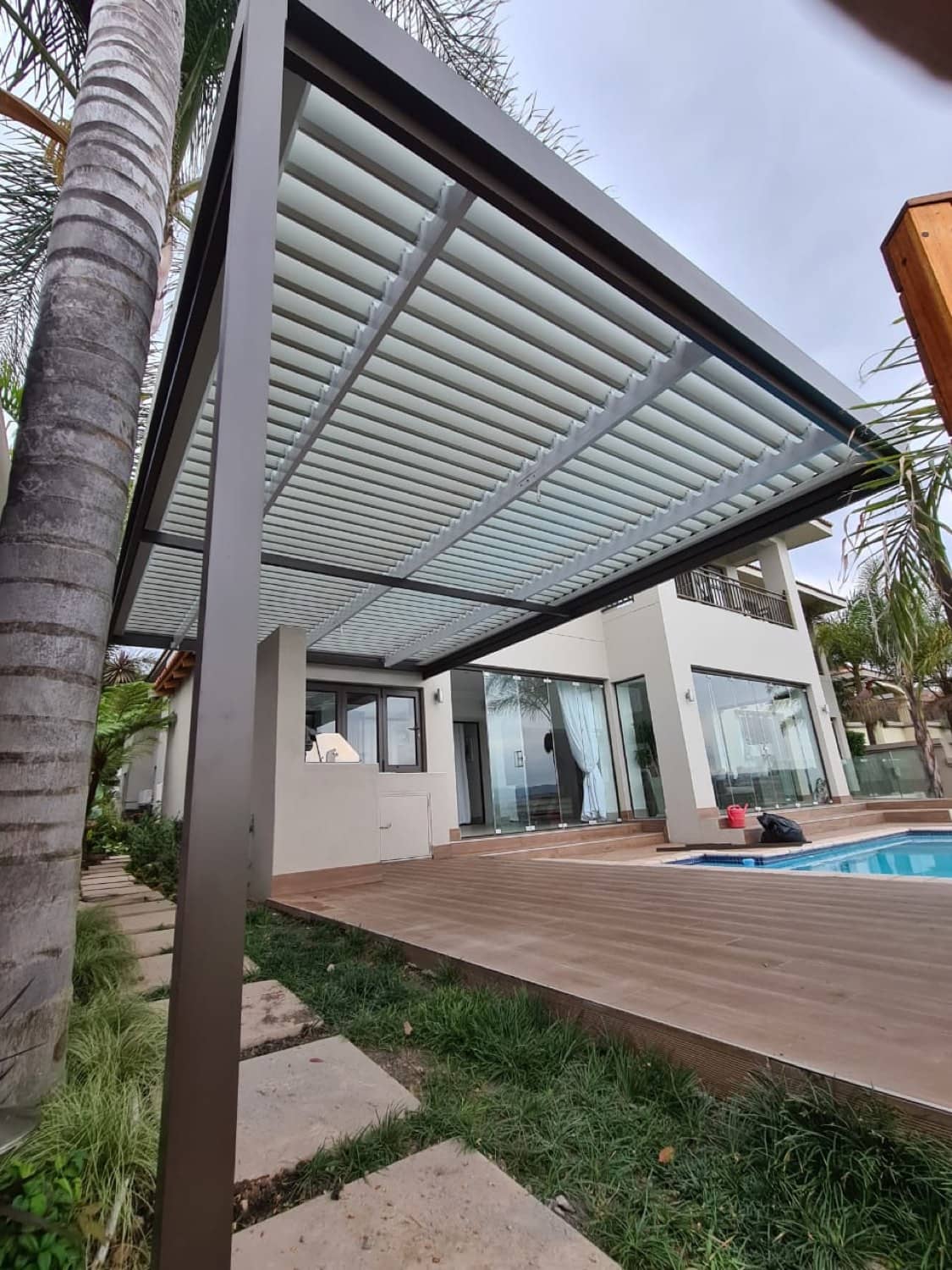 Bronze-framed louvre pergola with white slats over a timber pool deck