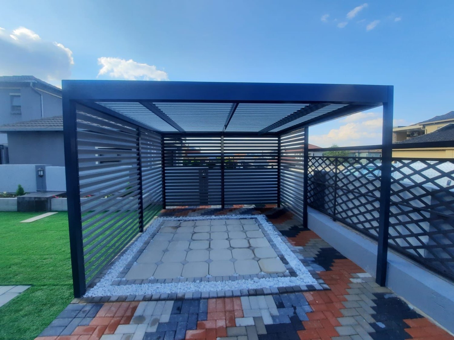 Freestanding charcoal louvre pergola with slatted privacy screens over a paved seating area