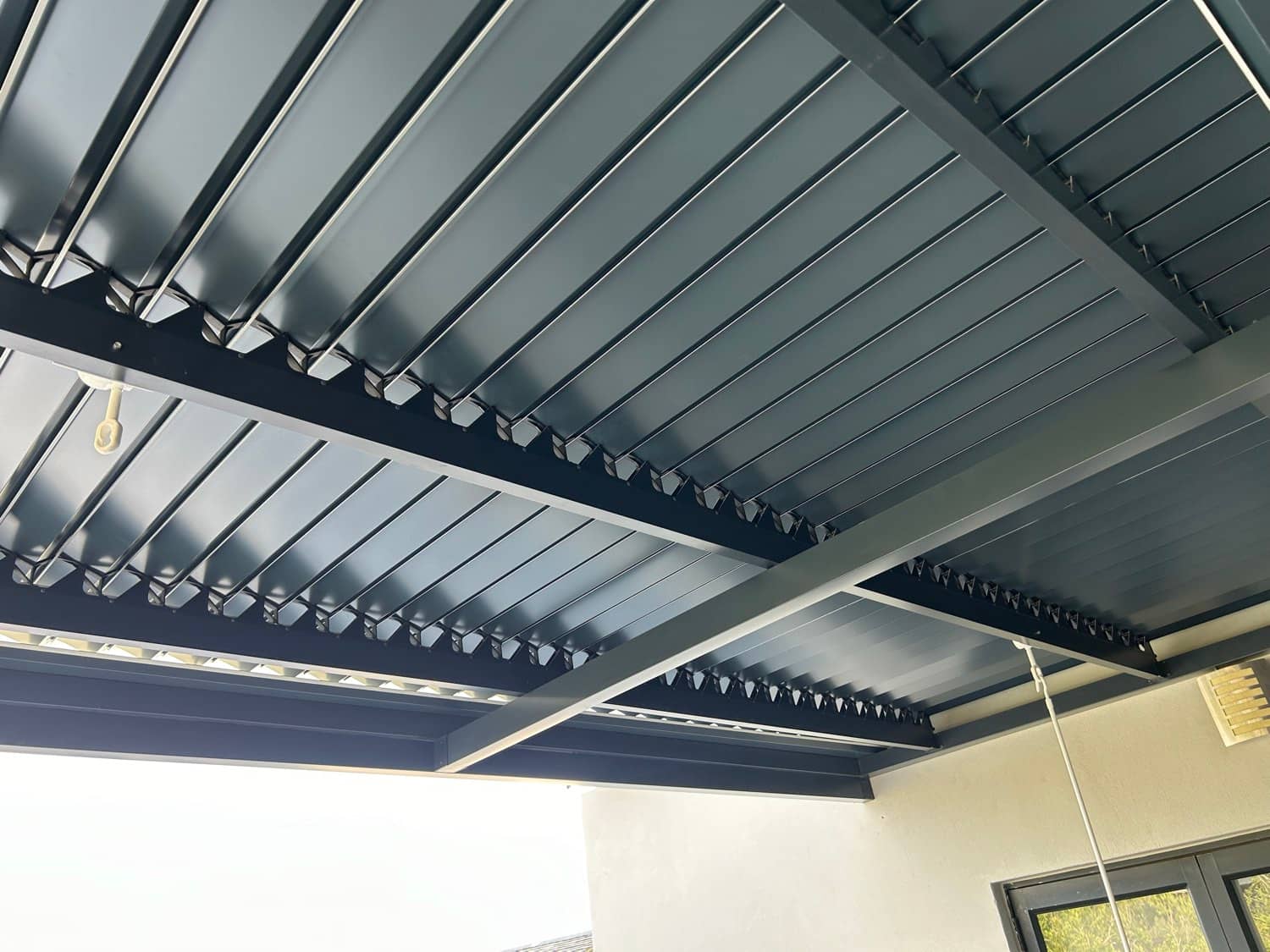 Underside of a charcoal louvre roof with slats fully closed, showing the beam structure