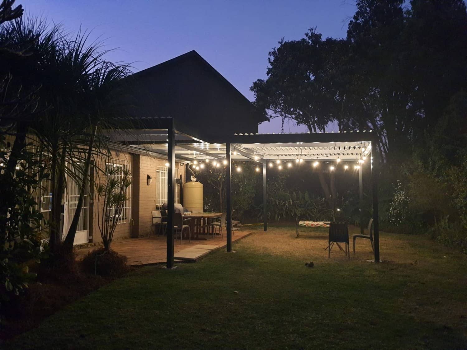 Louvre pergola strung with festoon lights over a garden patio at dusk