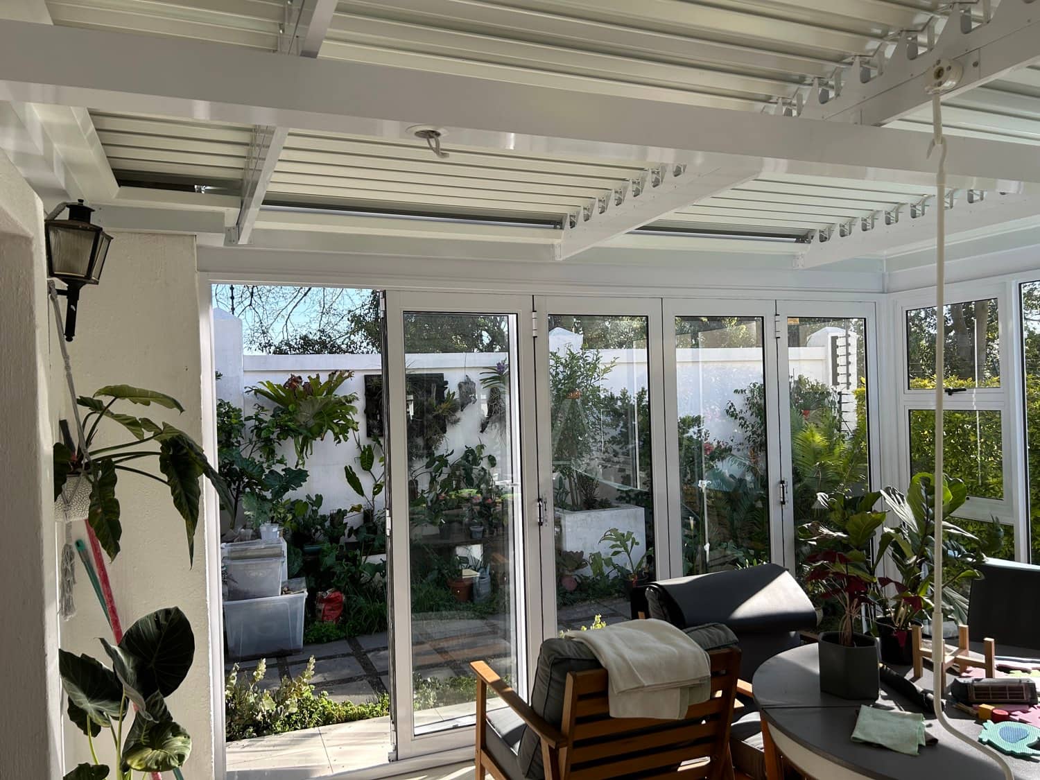 White louvre roof with slats tilted open above a bright garden room with white bifold doors