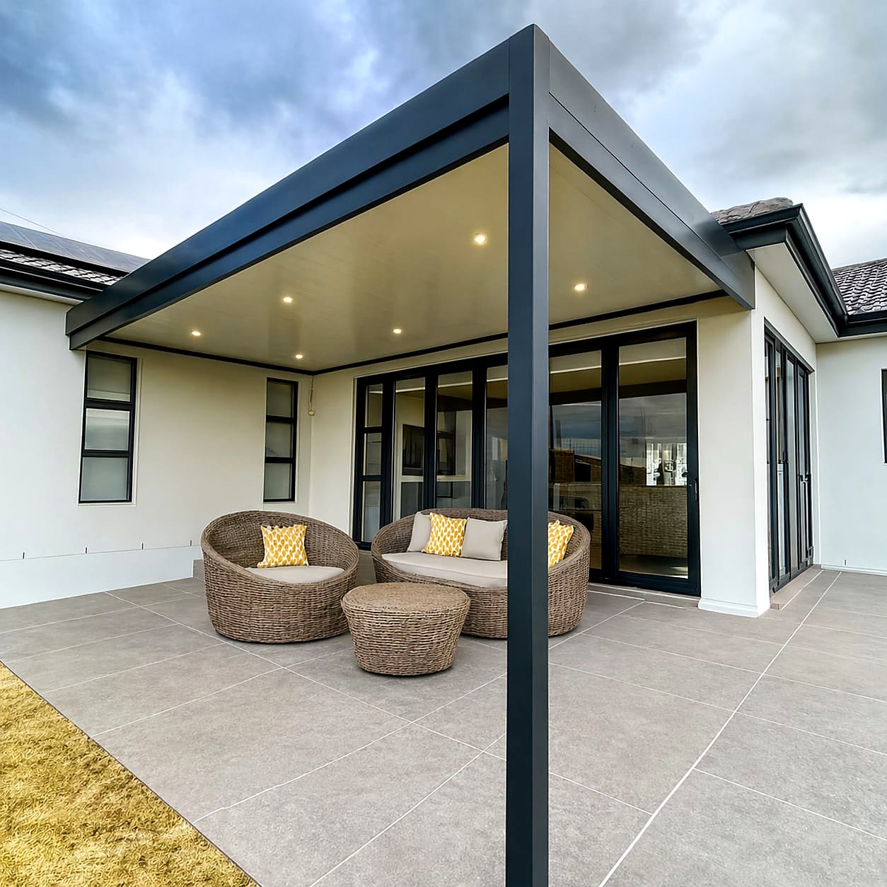 Charcoal aluminium patio cover with recessed downlights over an outdoor lounge in the evening