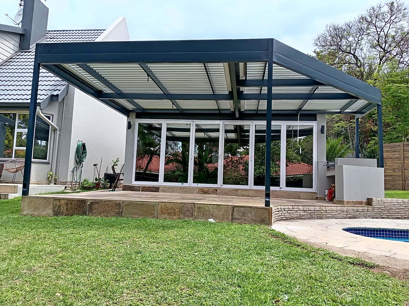 Charcoal aluminium structure with louvred roof over bi-fold doors and a lawn
