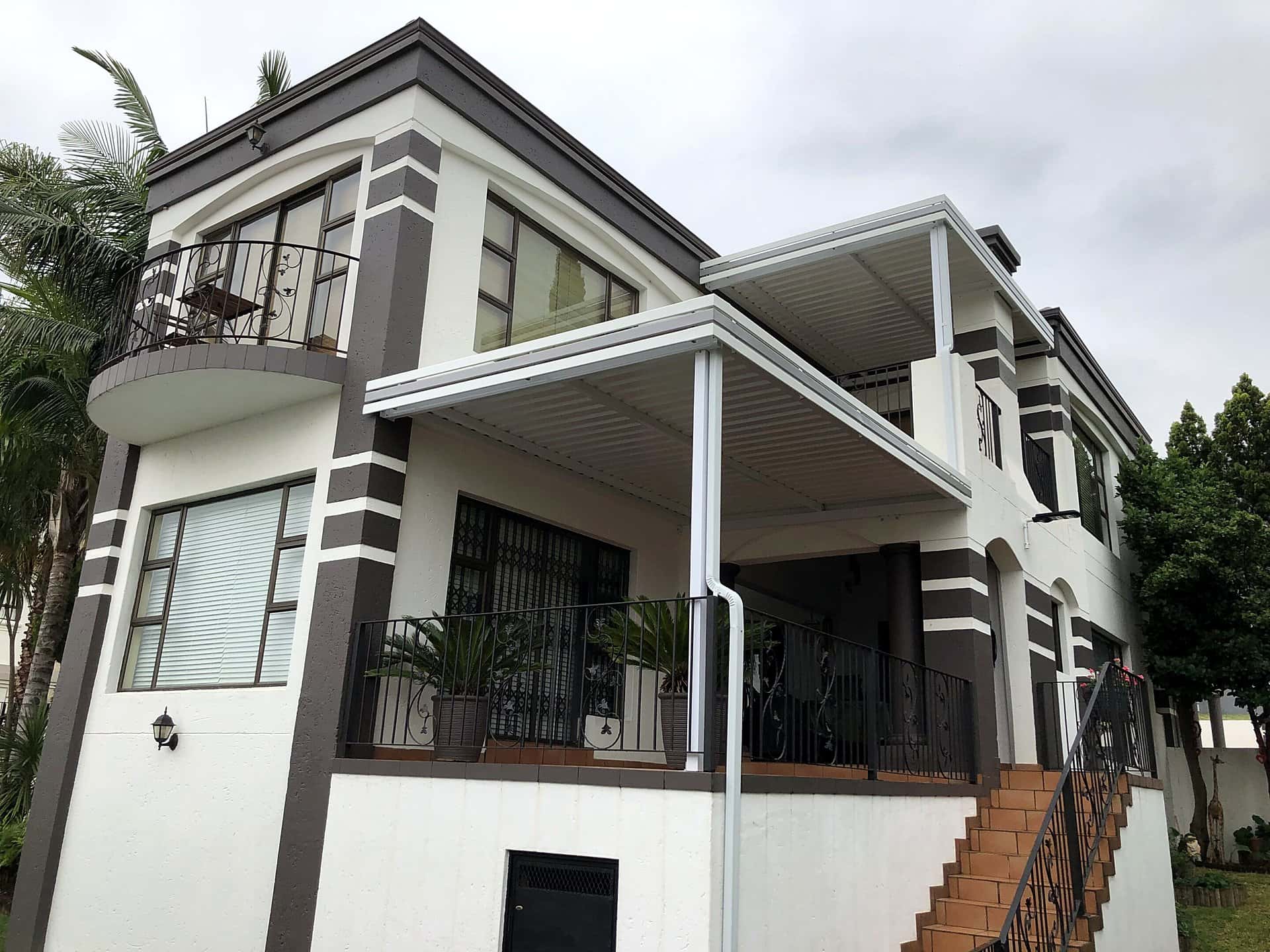 Twin white fixed awnings on the patio and balcony of a double-storey house