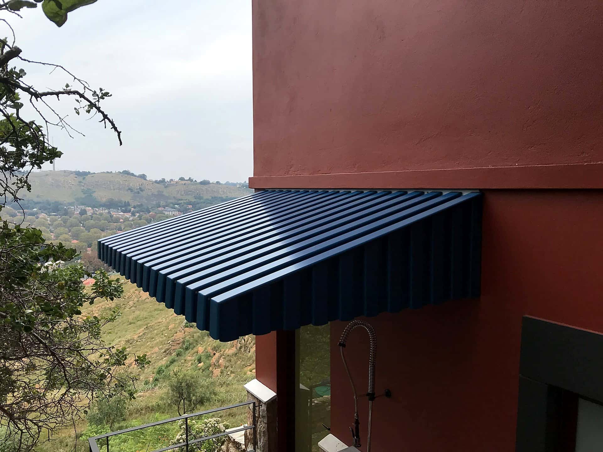 Blue louvred wedge awning mounted over windows facing a valley