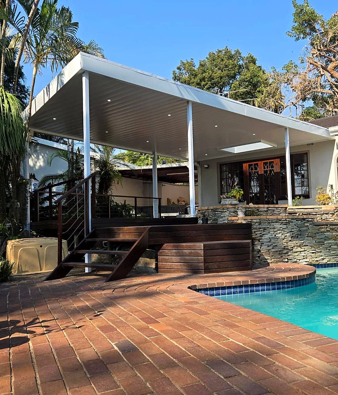 White aluminium patio cover beside a pool with palm trees