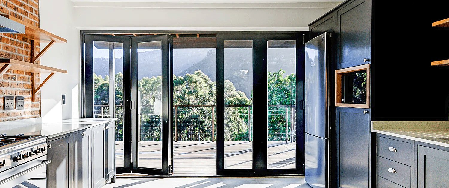 Black aluminium stacking doors open onto a deck with mountain views
