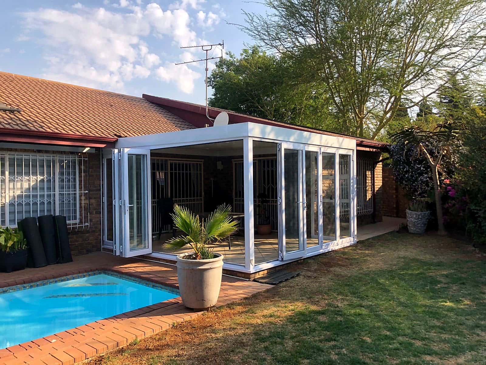 White aluminium stacking doors opening to a pool patio in golden-hour light