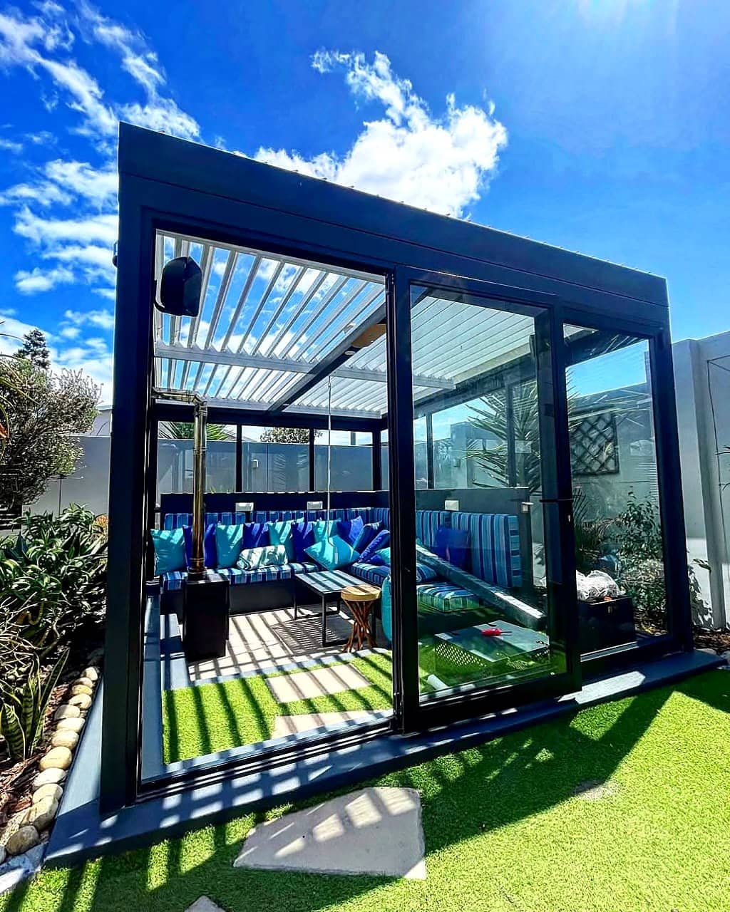 Freestanding louvre-roof pergola enclosed with glass panels around an outdoor lounge