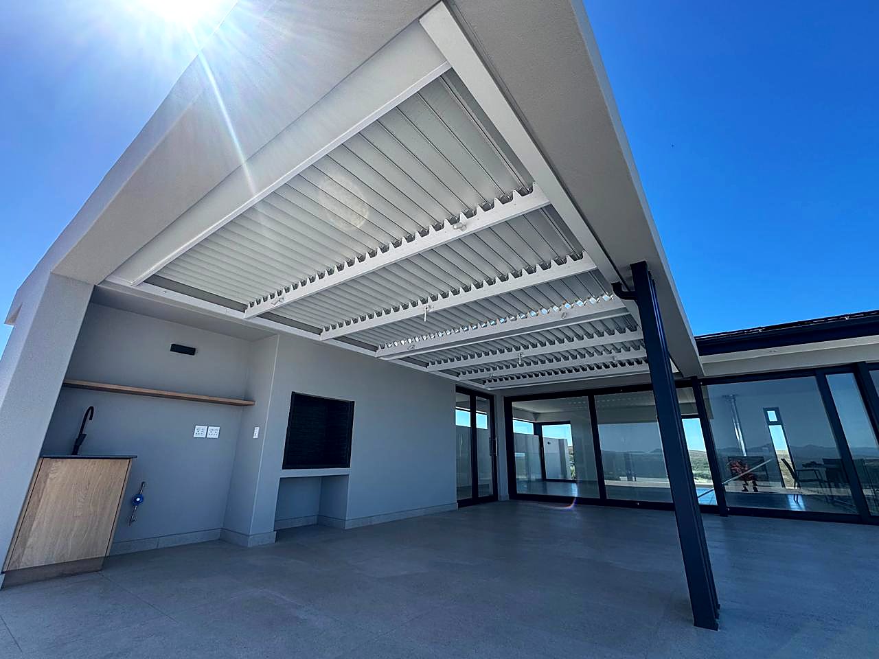 Closed louvre roof blades under a bright blue sky with sunburst