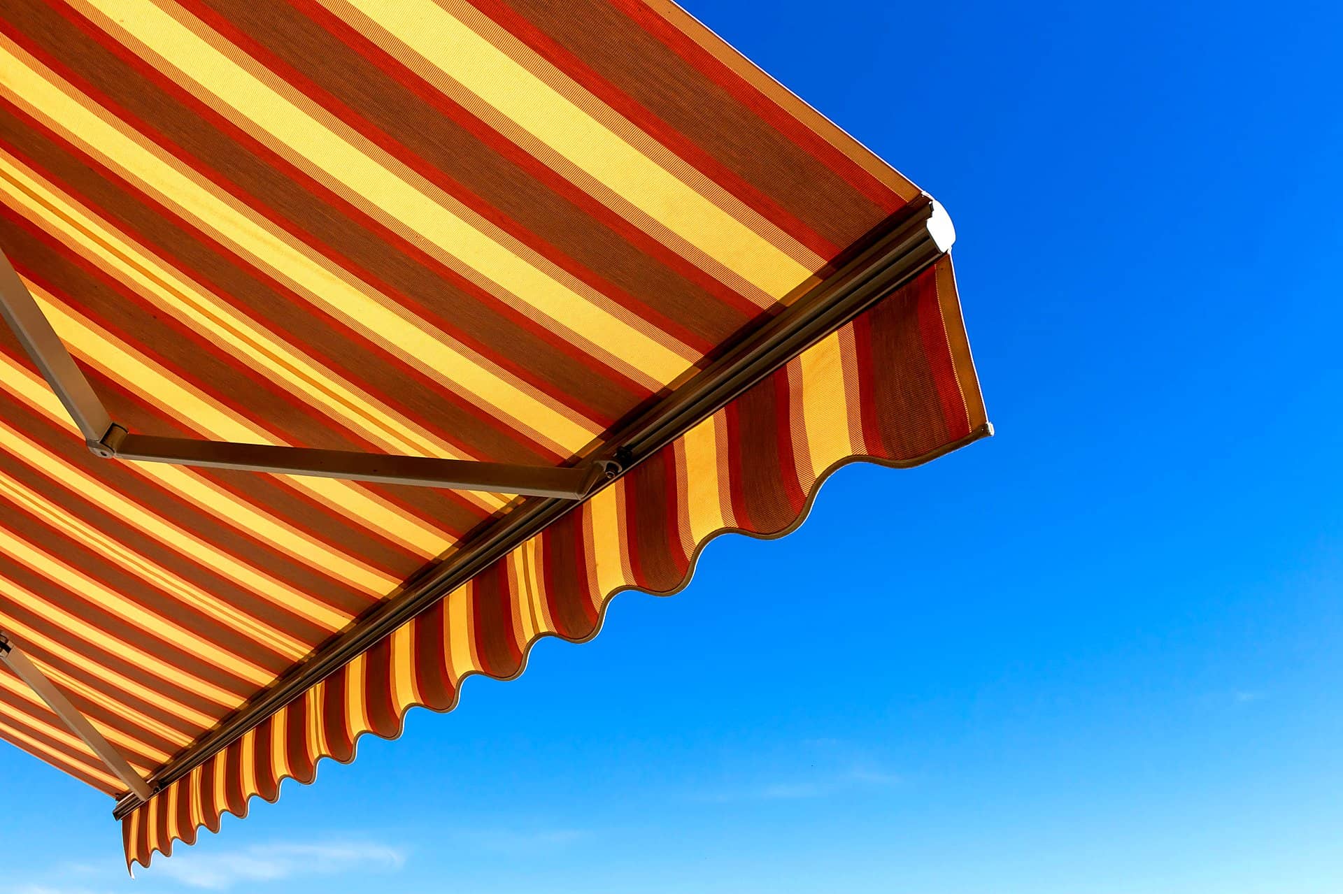 Striped canvas fold-arm awning extended against a clear blue sky