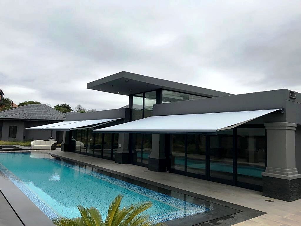 Twin grey fold-arm awnings shading a pool terrace at a luxury estate