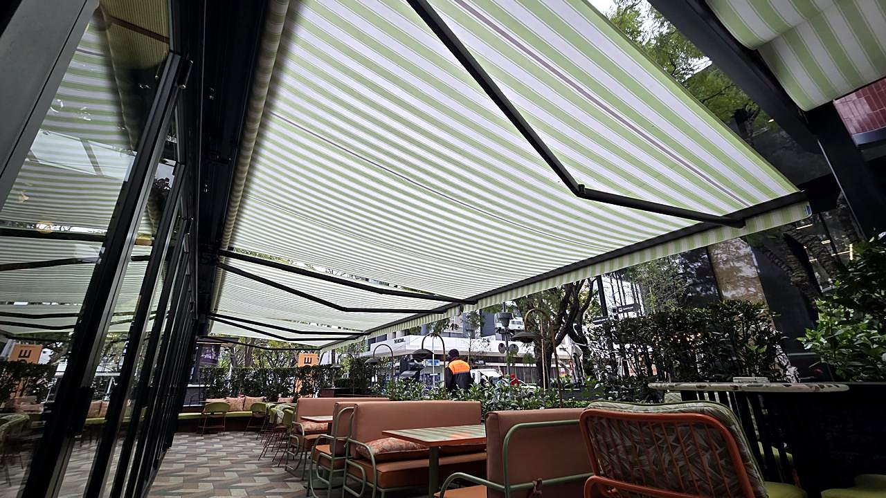 Green striped fold-arm awnings over an outdoor café terrace