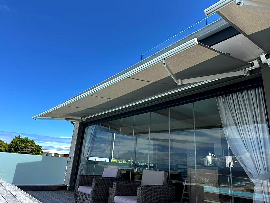 Taupe fold-arm awning on a modern glass beach house in Plettenberg Bay