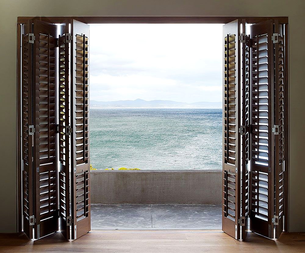 Dark bi-fold shutters folded back to frame an ocean view