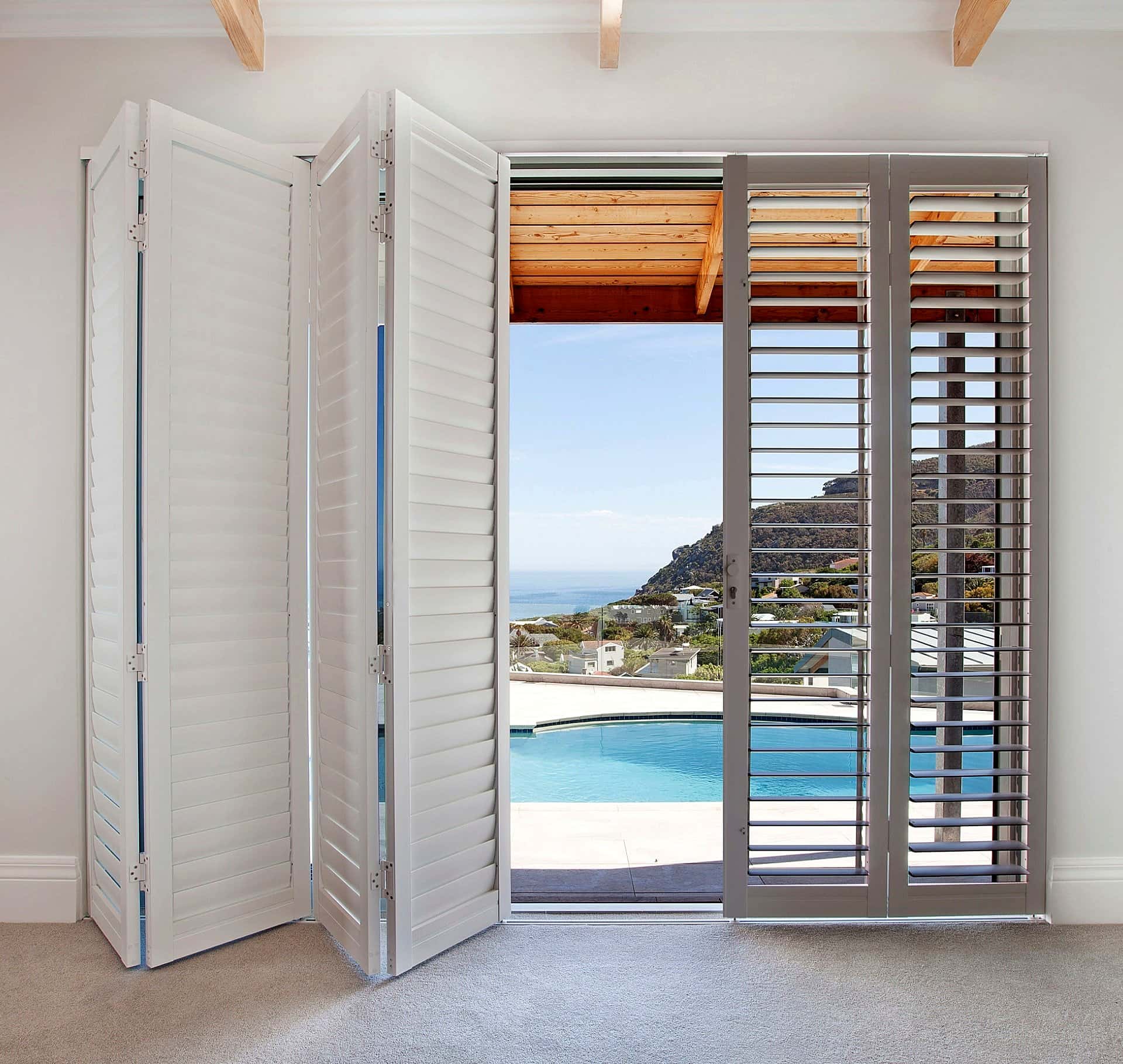 White bi-fold security shutters opening from a living room to a pool deck