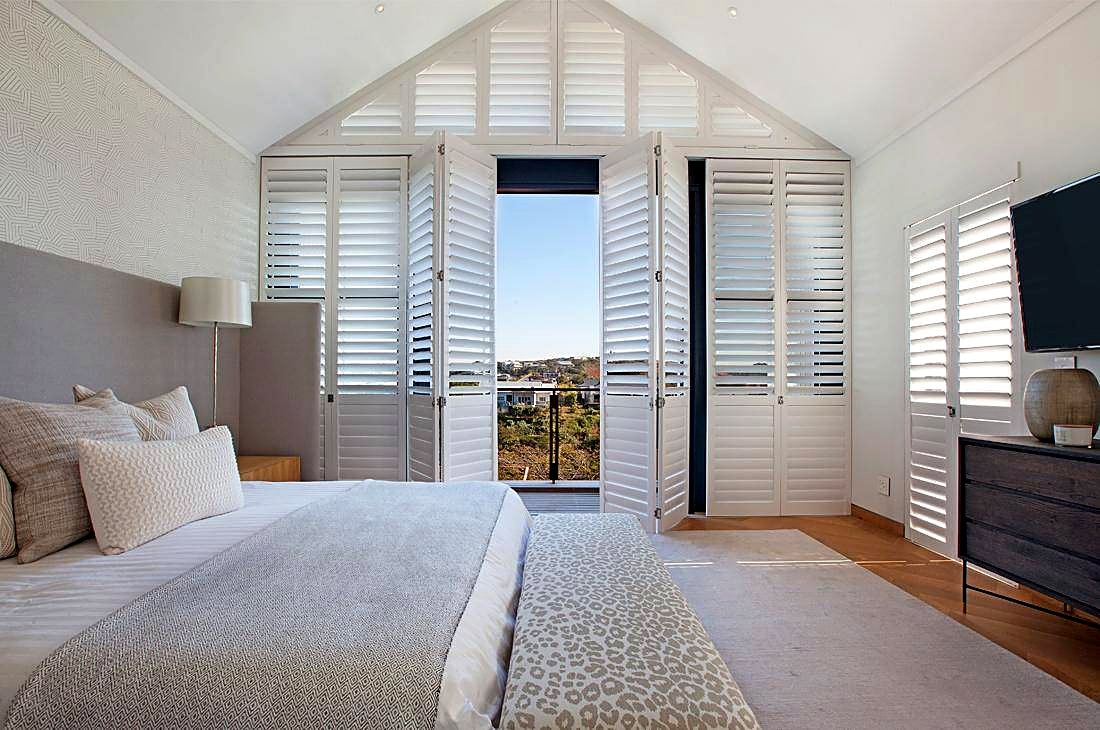 White special-shape shutters fitted to a gable window in a bright bedroom