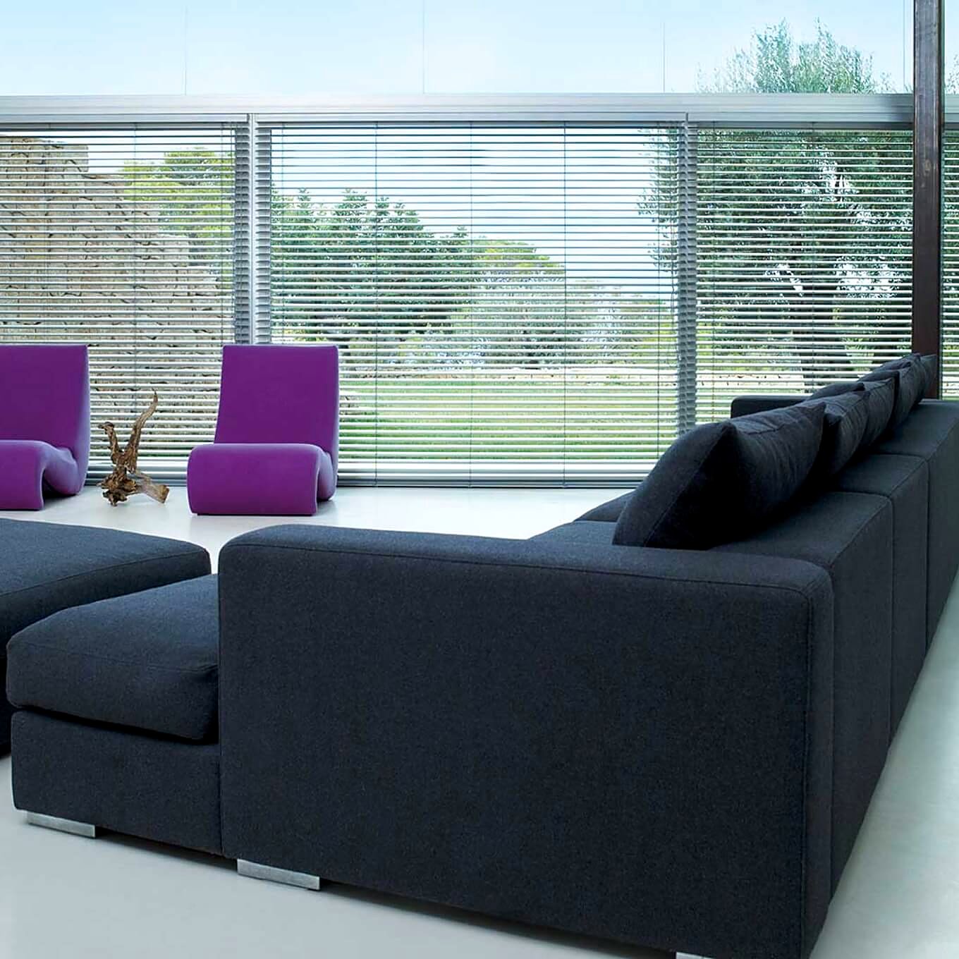 Silver aluminium venetian blinds spanning a floor-to-ceiling glass wall